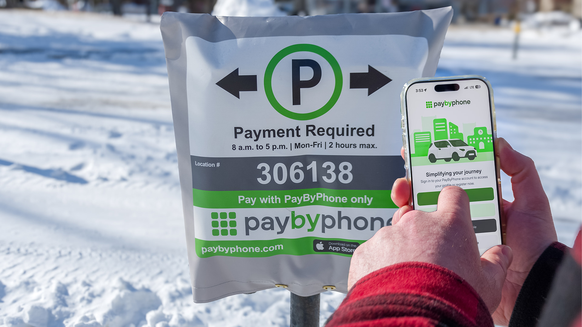A person holding their phone and using the PayByPhone app while looking at a parking meter with the PayByPhone sign and parking code on it.